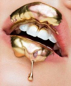 a woman's mouth with gold paint on it and dripping liquid coming out of the lip