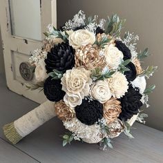 a bridal bouquet with black, white and gold flowers on a wooden table in front of a door