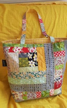 a large patchwork tote bag sitting on top of a yellow bed spreader