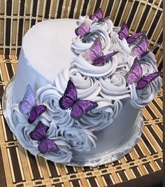 a cake with white frosting and purple butterflies on the top is sitting on a wicker chair