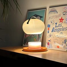 a desk lamp sitting on top of a wooden table next to a poster and plant