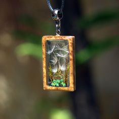 a dandelion in a wooden frame is suspended from a chain with green beads