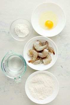 three bowls filled with different types of food on top of a white countertop next to an egg and flour