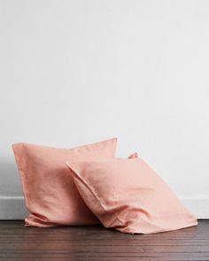 two pink pillows sitting on top of a wooden floor next to a white painted wall