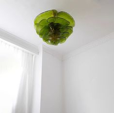 a green light fixture hanging from the ceiling in a room with white walls and curtains