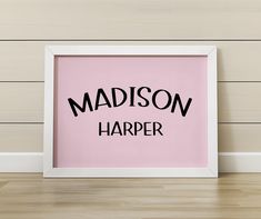 a framed pink poster with the words madison harper on it in front of a wooden wall