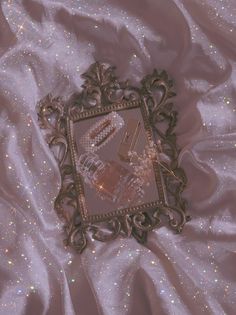 an ornate gold framed mirror on a white satin fabric with sparkles in the background