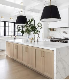 a large kitchen with marble counter tops and wooden cabinets, along with two hanging lights