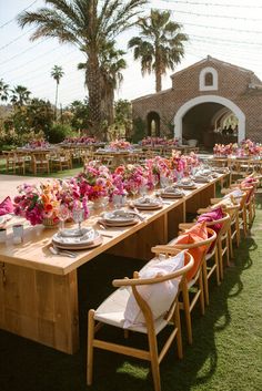 a long table set up with pink and orange flowers in vases, plates and silverware