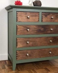 a green dresser with wooden drawers and knobs on the bottom drawer, in front of a white wall