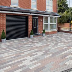 a brick driveway with two planters on each side and a black garage door in the middle