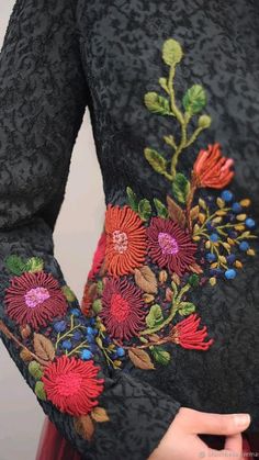 a woman wearing a black dress with red and pink flowers embroidered on the chestline