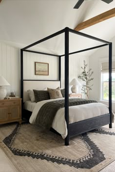 a bedroom with a four post bed and rugs on the floor in front of it