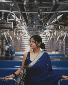 a woman in a blue sari is sitting on a train with her hand on the rail