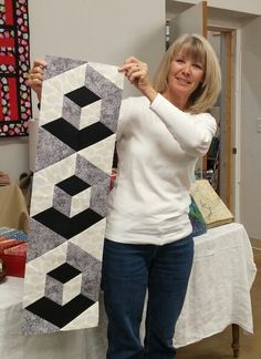 a woman holding up a piece of art made out of quilts on a table