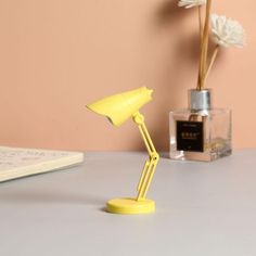 a yellow desk lamp sitting on top of a table next to a bottle of perfume