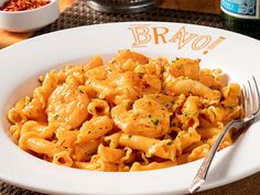 a white plate topped with pasta covered in sauce and parmesan cheese next to a bottle of beer