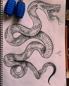 a pencil drawing of a snake on top of a piece of paper next to some markers