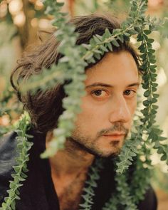 a man with long hair is looking at the camera through some green leaves on his head