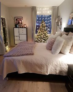 a bedroom decorated for christmas with a tree in the window and lights on the wall