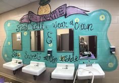 there are three sinks in the bathroom with writing on the wall above them, and two urinals below