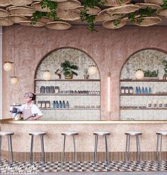 a woman sitting at a bar in front of two windows with plants hanging from the ceiling