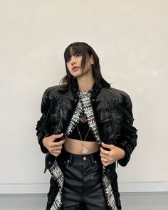 a woman standing in front of a white wall wearing black leather pants and a crop top