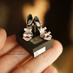 a miniature pair of baby shoes sitting on top of a black shoe box in someone's hand