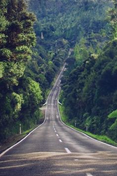 an empty road surrounded by trees and hills