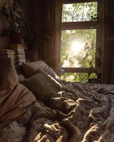 the sun shines through an open window onto a bed with pillows and blankets on it