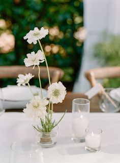 white flowers are in vases on a table with candles and napkins around it