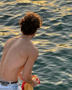 a shirtless man sitting on top of a boat in the water