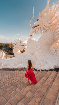 a woman in a red dress standing next to a white dragon statue