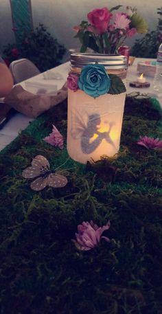 a jar filled with flowers sitting on top of a moss covered table next to a candle