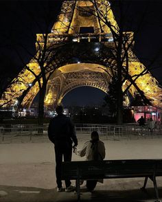 two people sitting on a bench in front of the eiffel tower at night