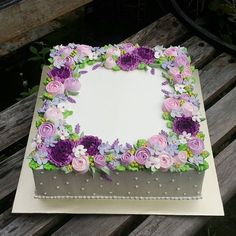 a square cake decorated with flowers on top of a wooden table next to a bench