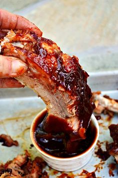 a person dipping ribs into a small bowl of barbecue sauce