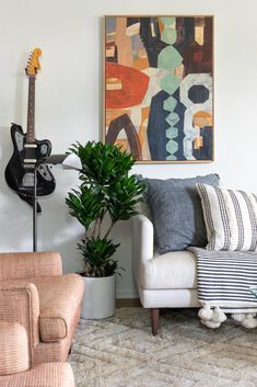 a living room filled with furniture and a guitar hanging on the wall next to a potted plant