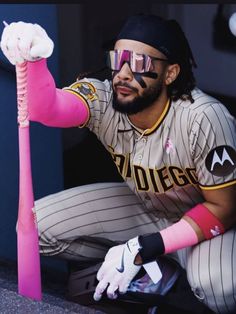 a baseball player holding a pink bat in his right hand and wearing goggles on