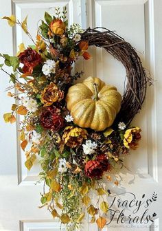 a wreath with flowers, leaves and a pumpkin on it is hanging from the front door