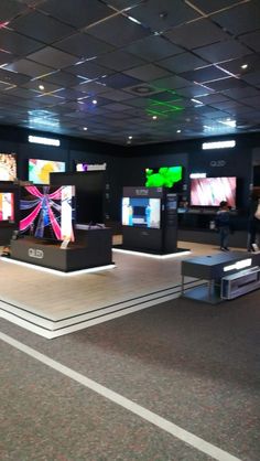 an empty room with several televisions on the wall and people standing around it in front of them