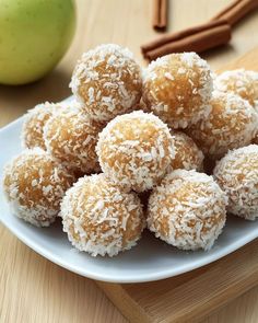 a plate full of coconut balls on a table next to an apple and cinnamon sticks