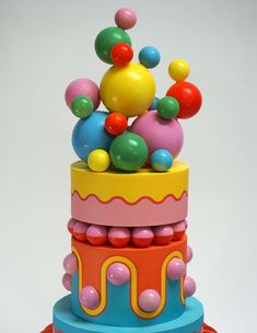 a multi - colored cake with lots of colorful balls on top, sitting in front of a white background