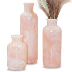 three pink vases with feathers in them