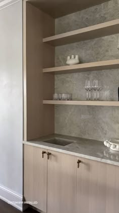 an empty kitchen with marble counter tops and shelves filled with glasses, plates and bowls