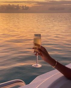 a person holding a glass of wine on a boat in the ocean at sunset or sunrise