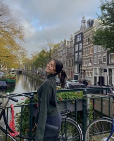 a woman standing next to a bike on a bridge over a canal in the city