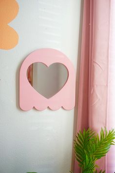 a pink heart shaped mirror mounted to the side of a wall next to a potted plant