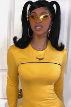 a woman in a yellow dress with gold sunglasses on her face and long black hair