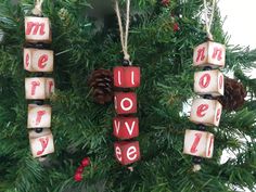 christmas ornaments hanging from a tree with the word love spelled in blocks and pine cones